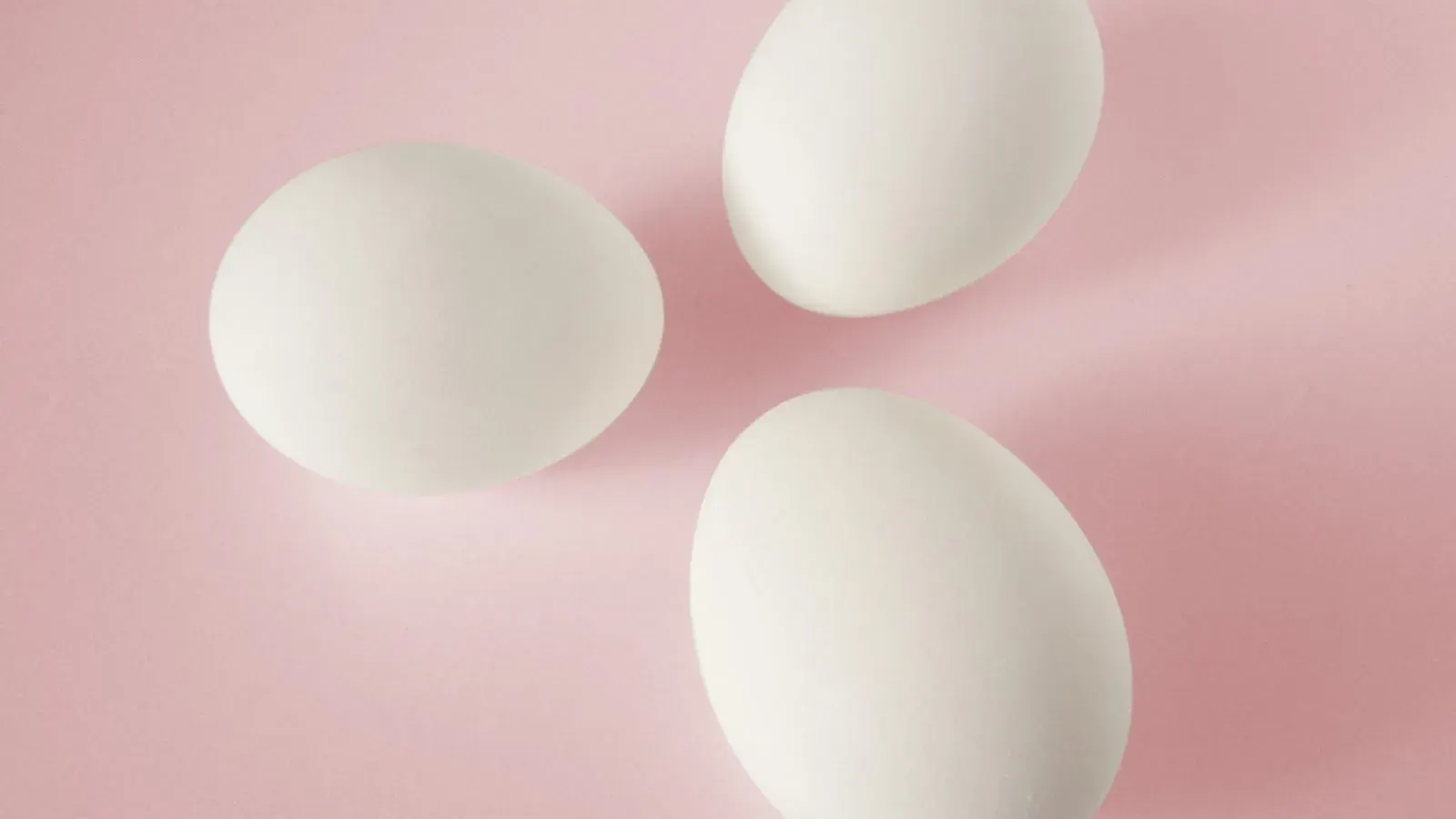 A group of pale chicken eggs photographed close together on a plain surface