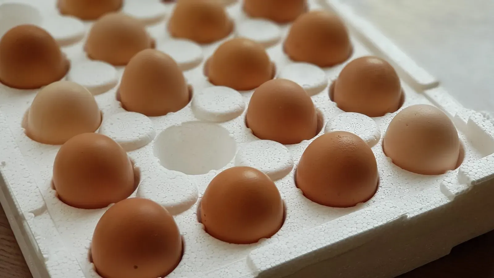 A wire basket of freshly collected brown eggs on a farm table