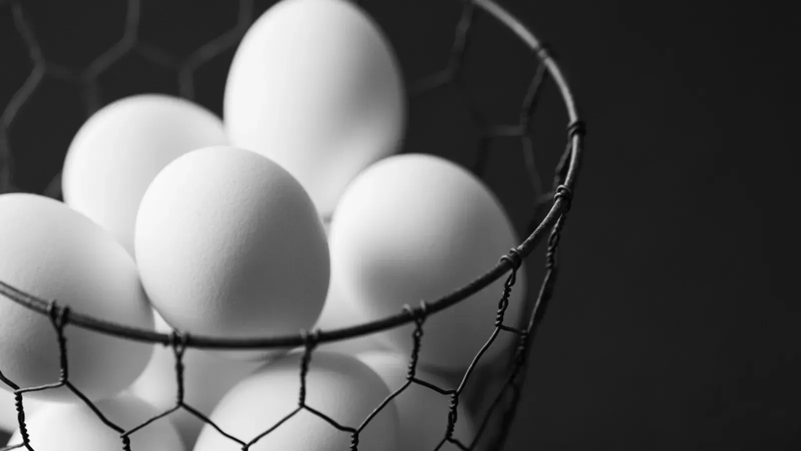 A wire basket of freshly collected brown and white eggs on a wooden surface